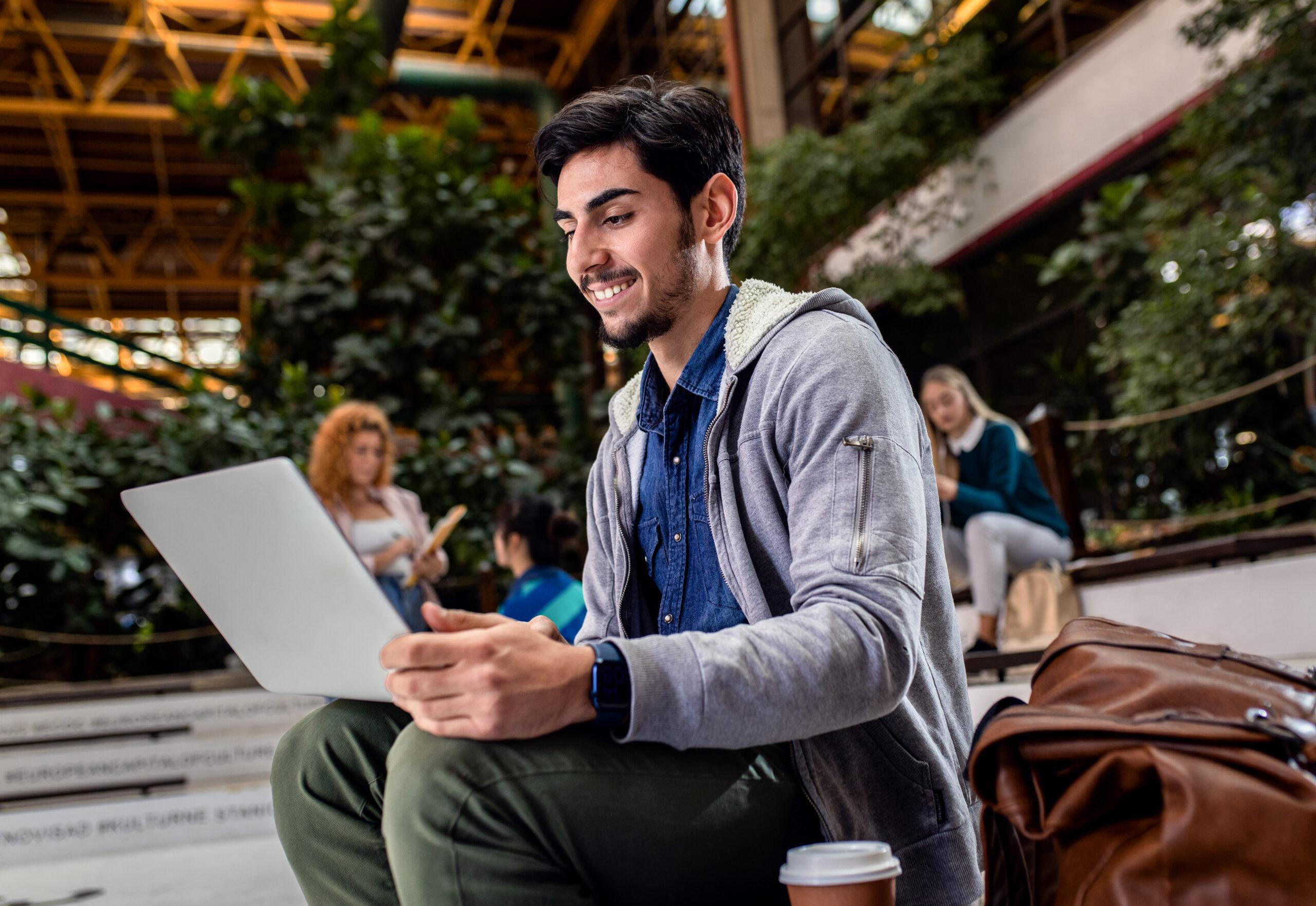 Portrait of male student siting in campus using laptop.