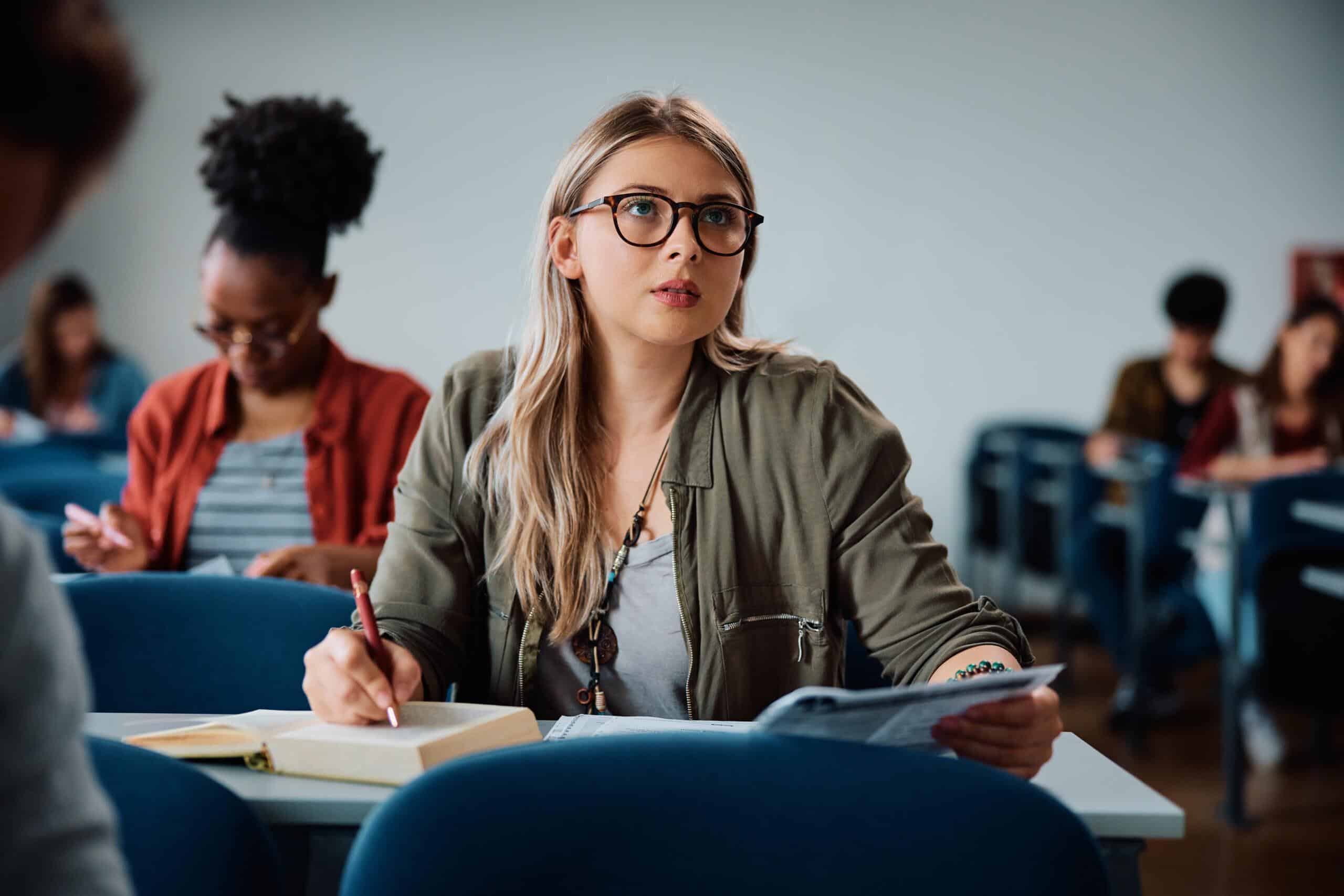 University student writing in her notebook during a class at lecture hall.